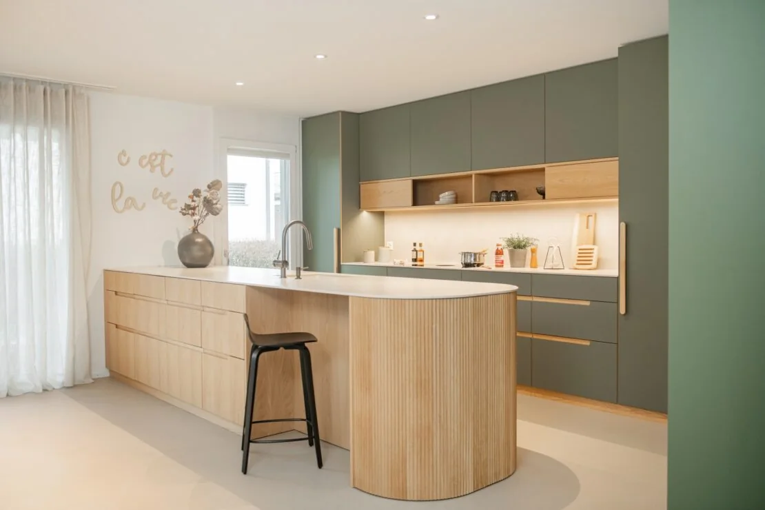Cuisine verte et bois avec îlot arrondi et plan clair en Dekton Albarium.