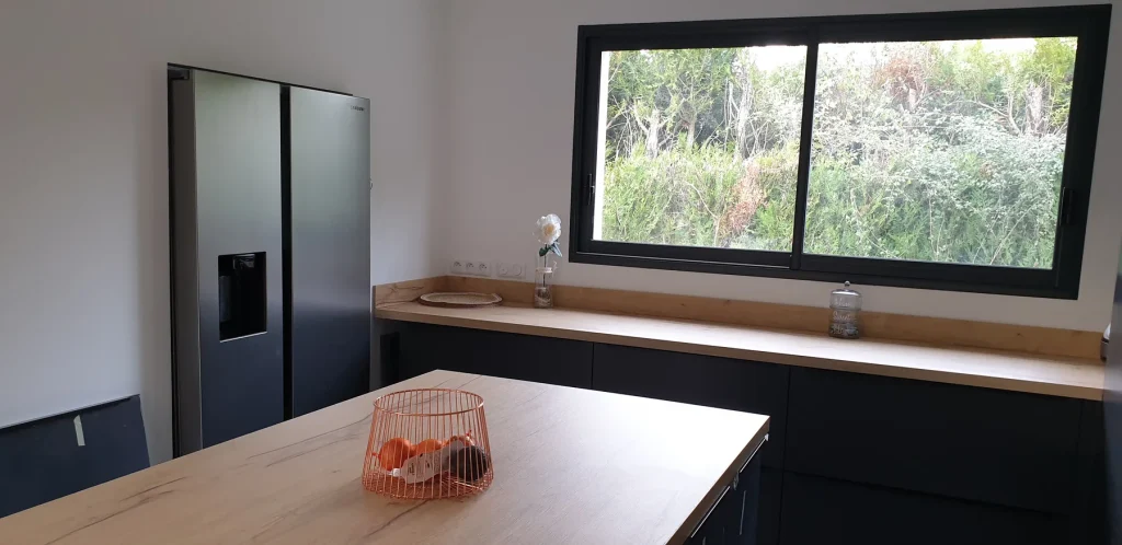 Cuisine noire avec îlot bois sous une grande fenêtre
